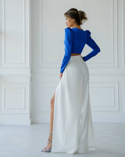 Woman wearing a blue top and white skirt in a room with white walls.