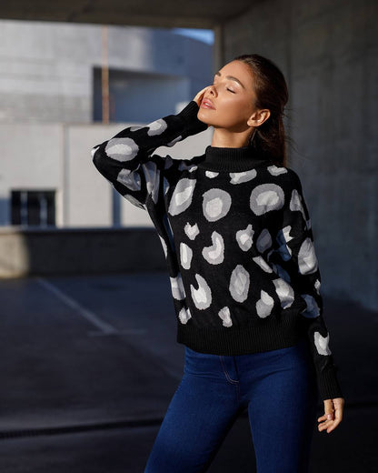 Woman wearing a black sweater with white abstract patterns and blue jeans in an urban setting.
