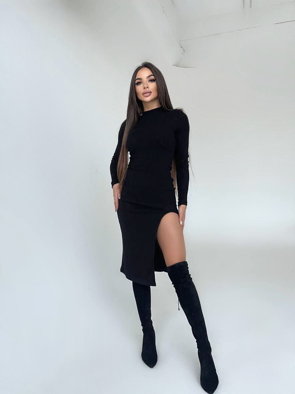 Woman wearing a black dress with a slit and black knee-high boots against a white background