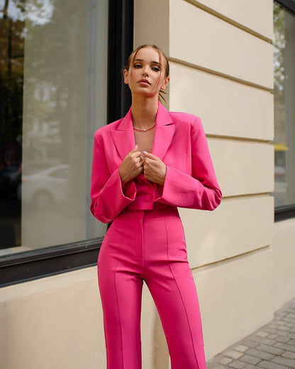 Woman wearing a bright pink suit standing against a building.