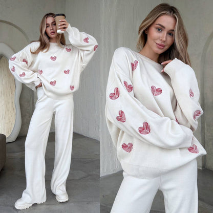 Woman wearing a white sweater with red heart patterns in a modern interior setting.