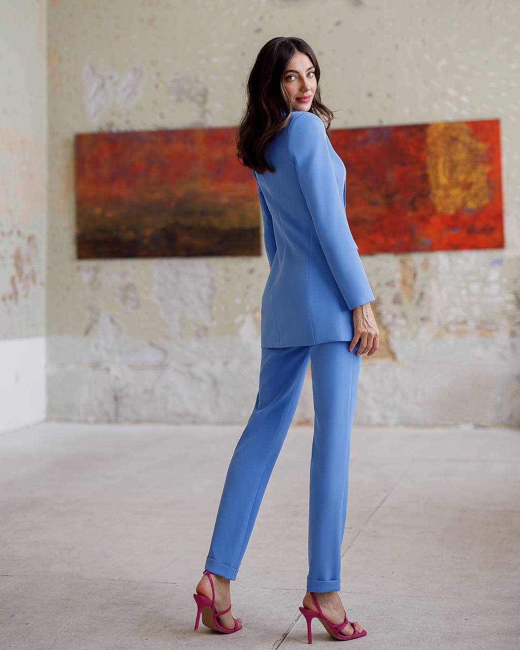 Woman in a blue suit standing in a room with abstract art on the wall.