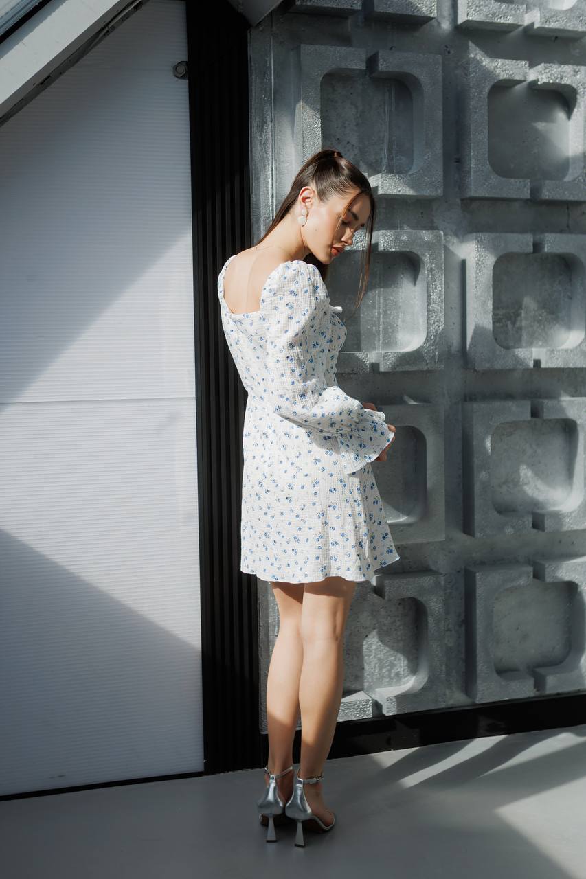 Woman in a white floral dress standing against a textured wall.