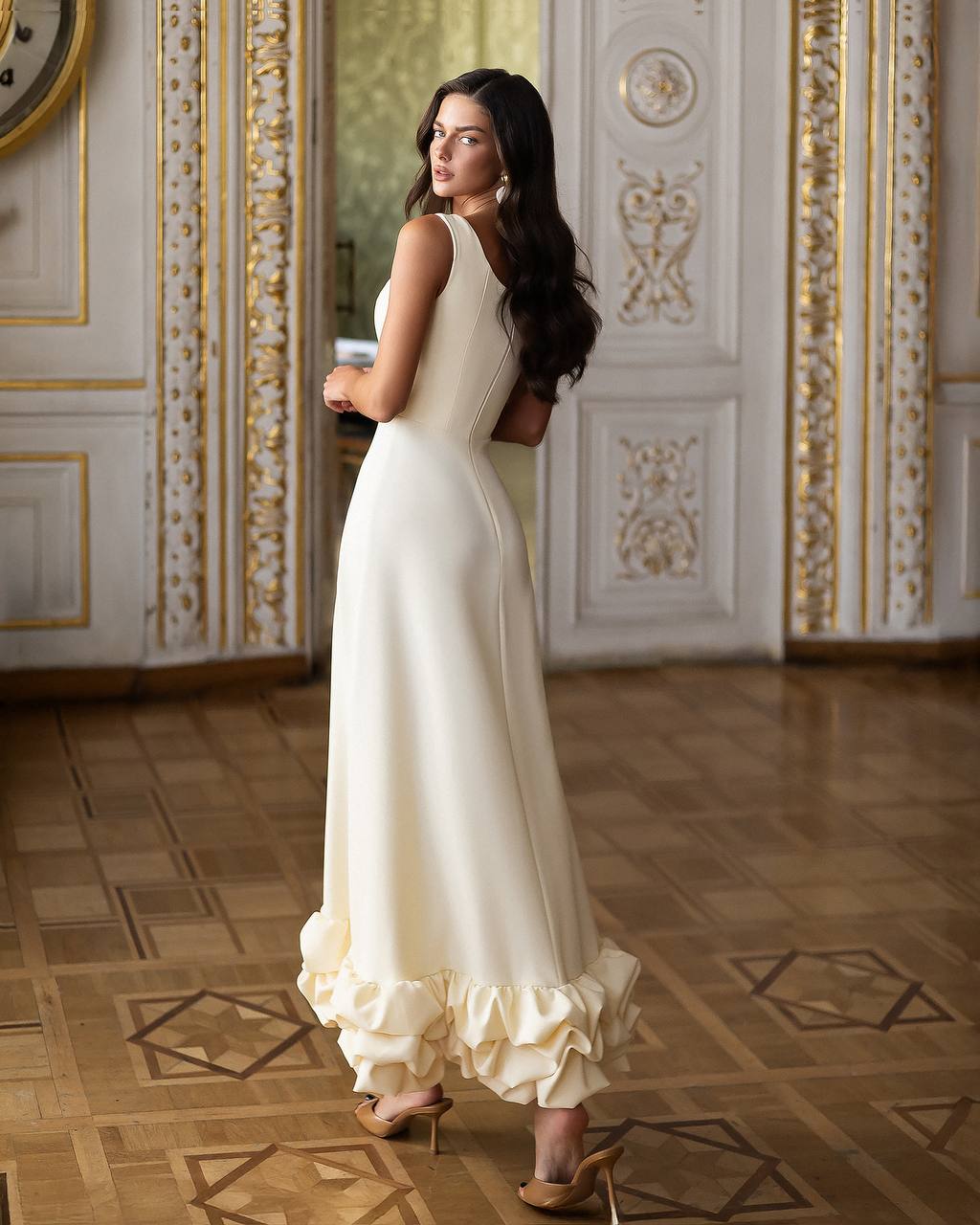 Woman in a white dress standing in an ornately decorated room.