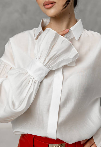 White blouse with ruffled details worn by a person against a neutral background
