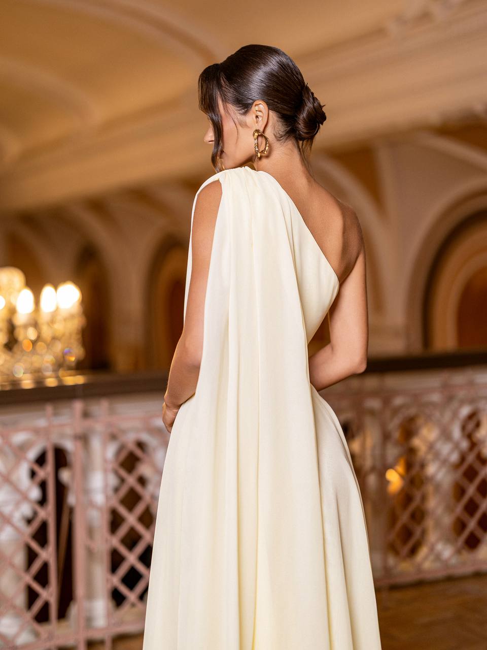 Woman in a white evening gown standing in an elegant indoor setting.