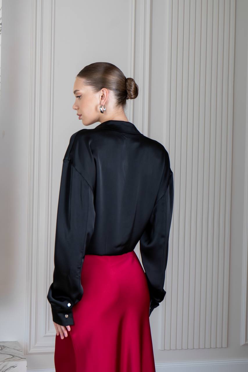 Person wearing a black blouse and red pants against a white paneled wall.