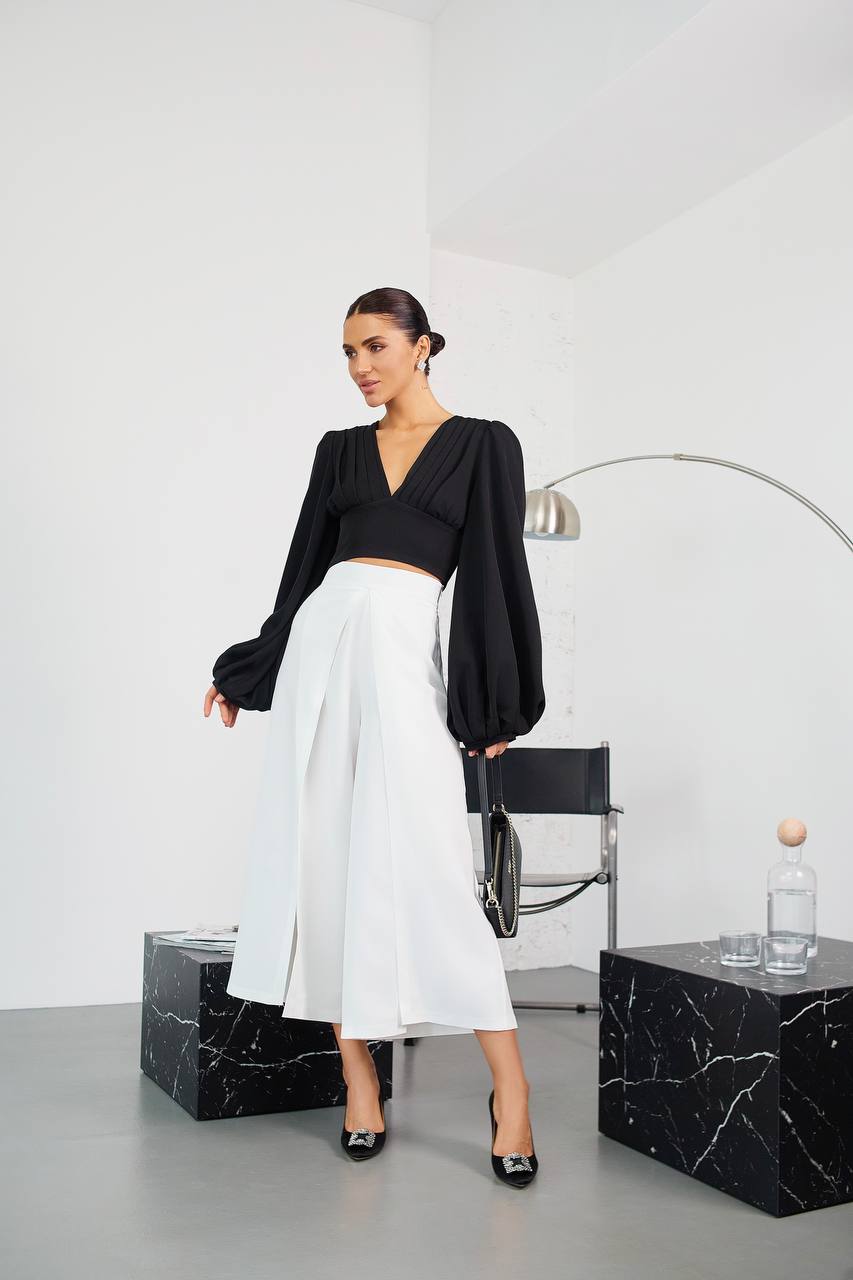 Woman in black top and white skirt standing in a modern room with marble furniture.