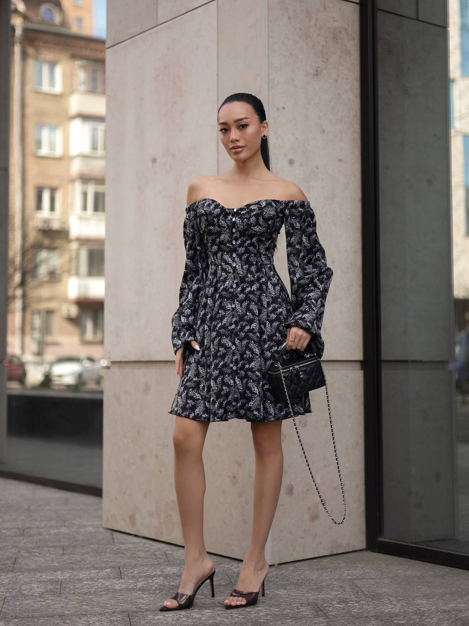 Woman in a floral off-shoulder dress standing against a concrete wall.