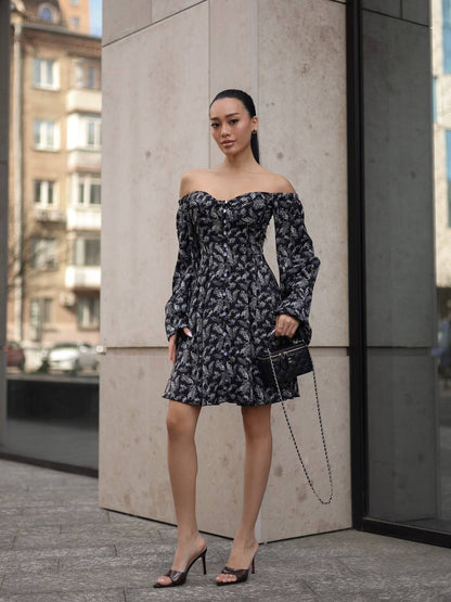 Woman in a floral off-shoulder dress standing against a concrete wall.