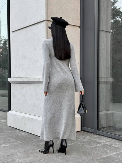 Woman in a long gray dress standing outside a modern building.