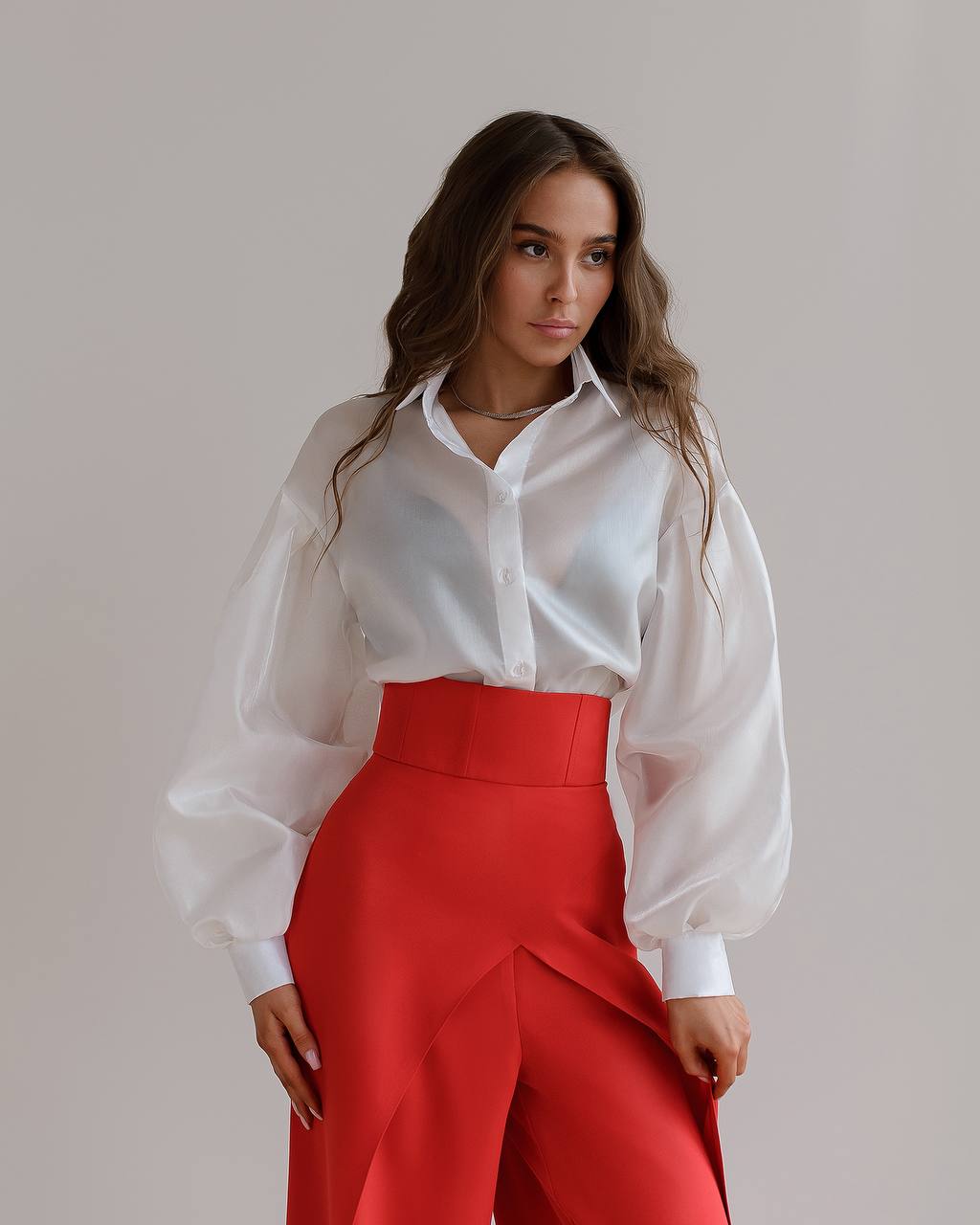 Woman wearing a white blouse and red pants against a plain background