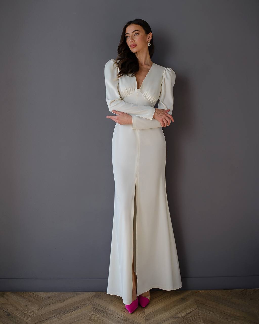 Woman wearing a white dress with puffed sleeves against a gray wall.