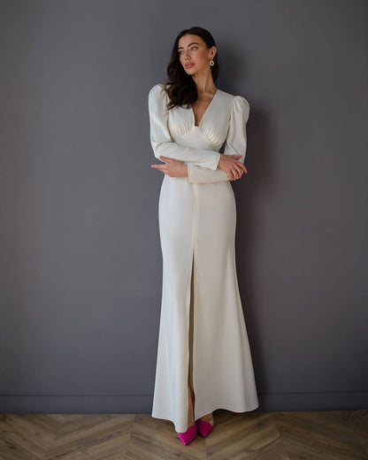 Woman wearing a white dress with puffed sleeves against a gray wall.
