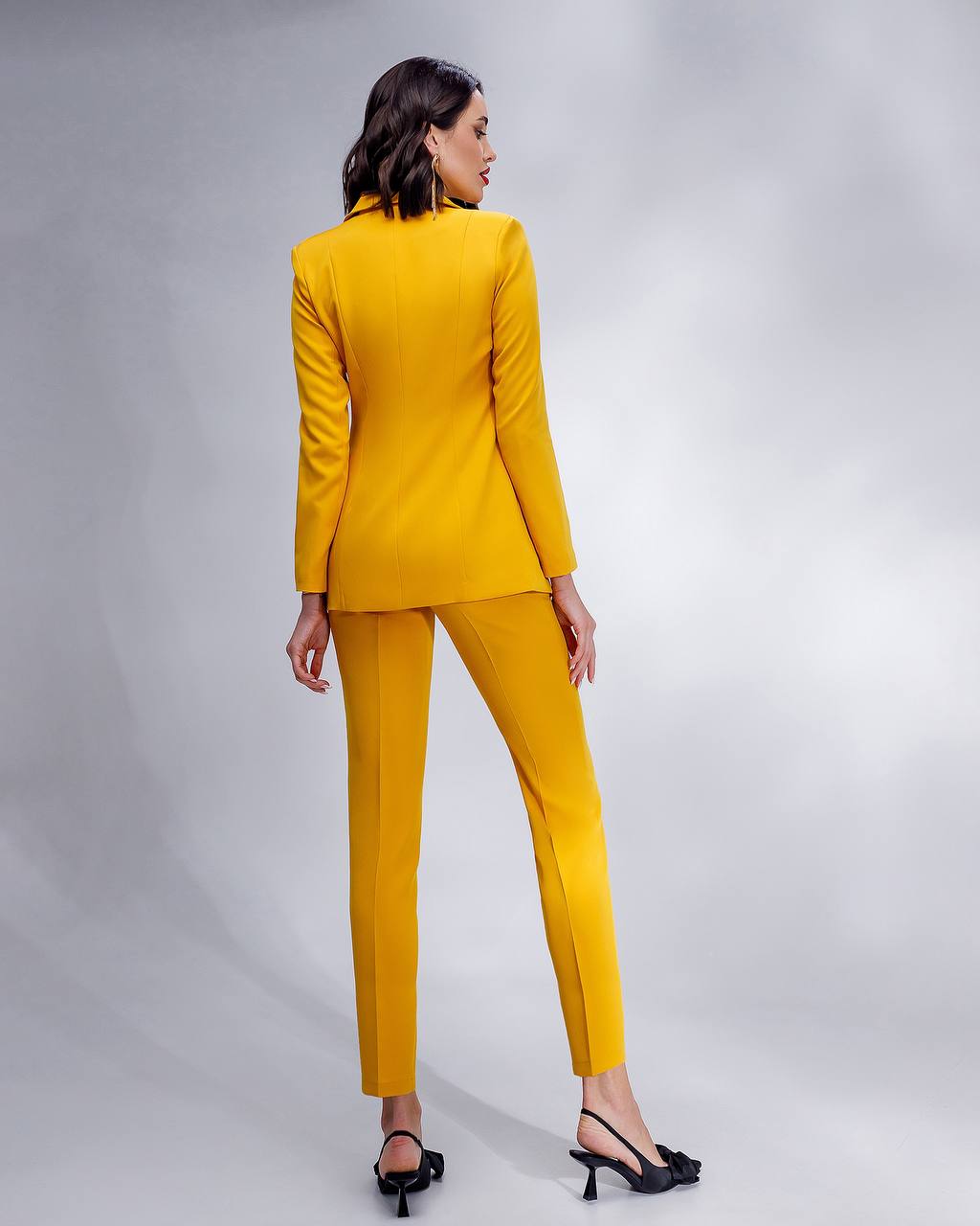 Woman wearing a yellow suit standing against a gray background