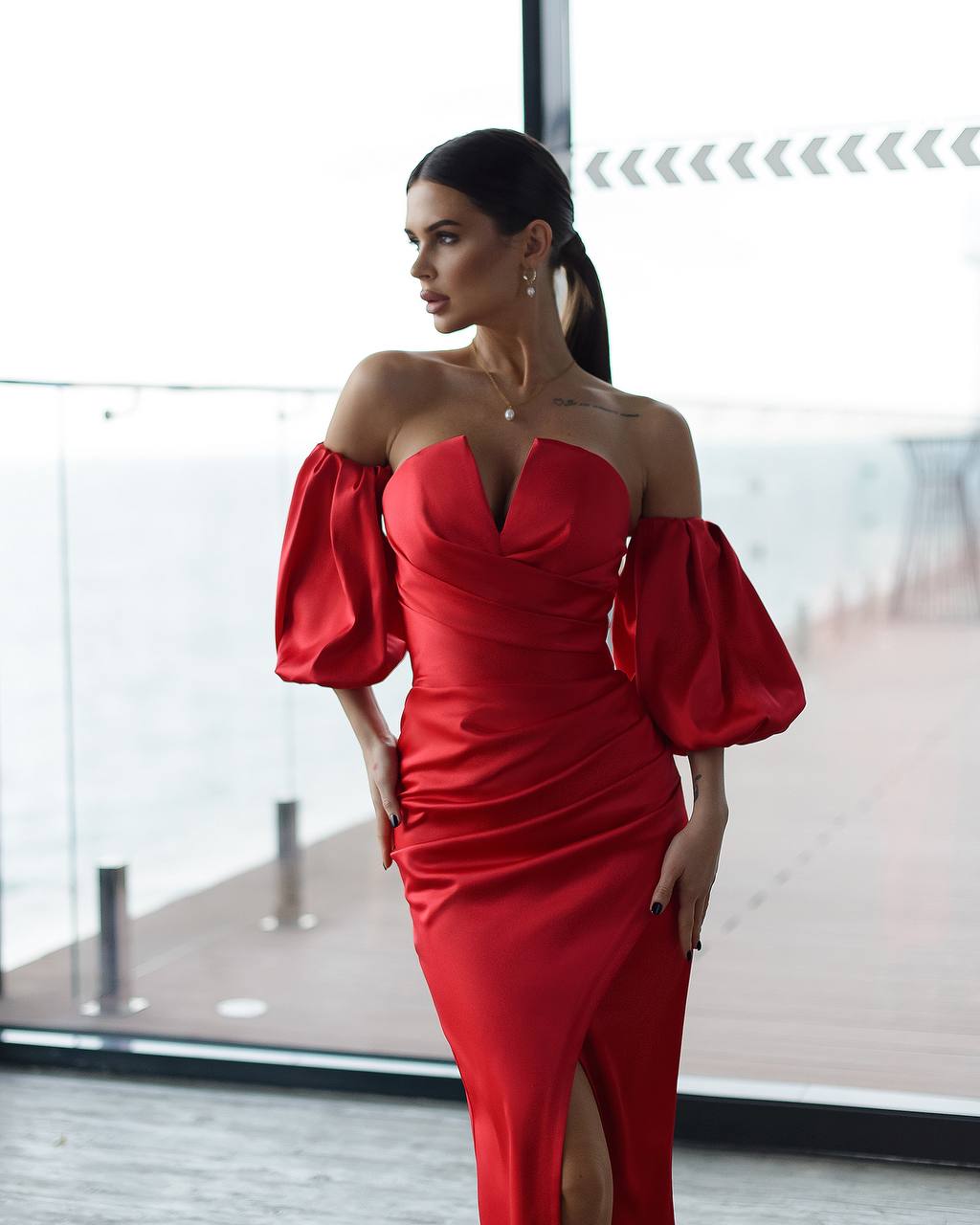 Woman wearing a red off-shoulder dress with puffed sleeves in an indoor setting.