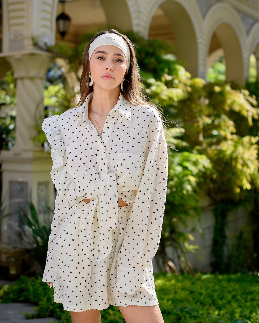 Woman wearing a white polka dot dress with a headband in an outdoor setting