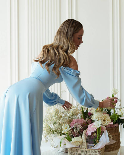 Woman in a light blue dress arranging flowers in a room with white walls.