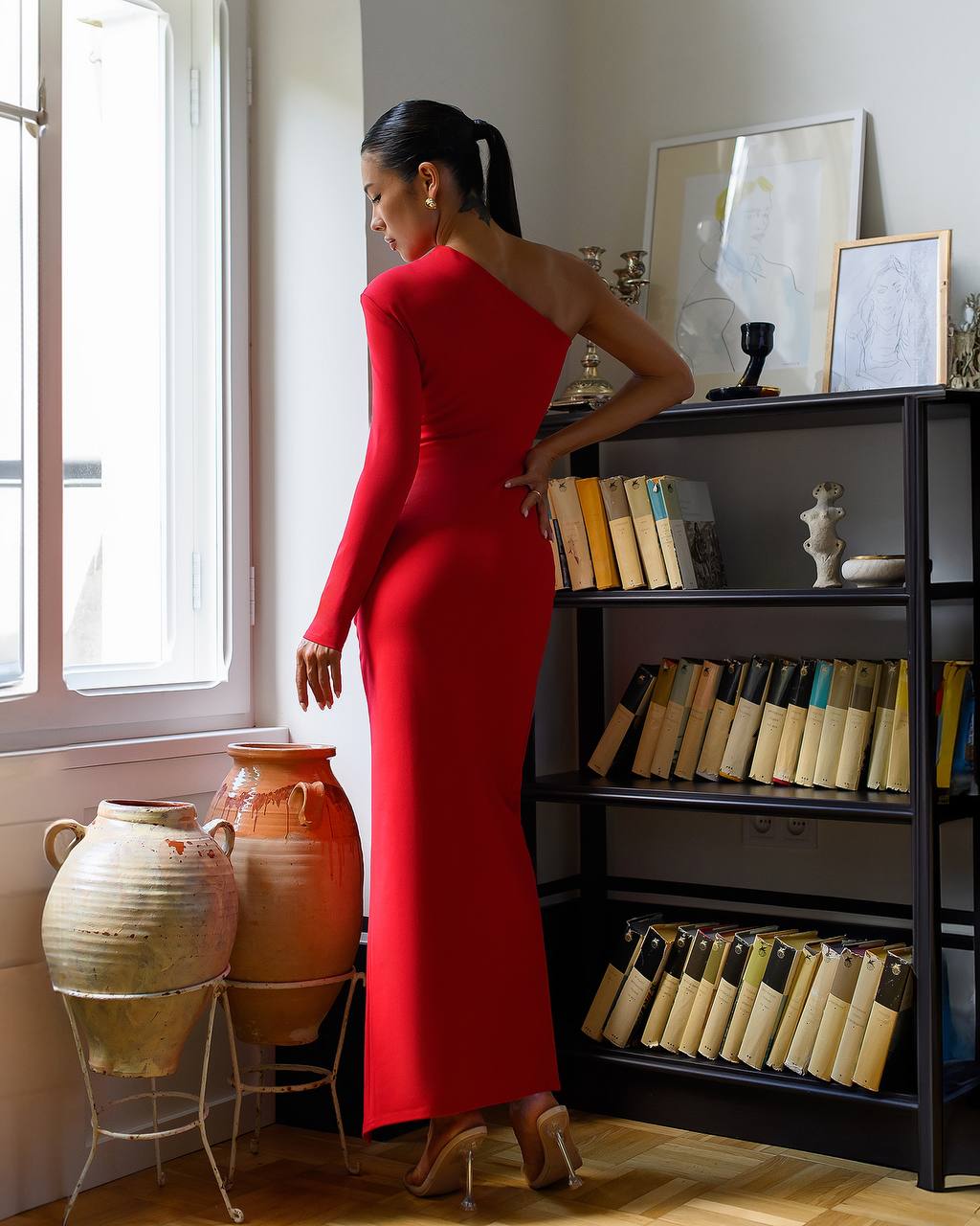 Woman in a red dress standing in a room with a bookshelf and decorative vases.