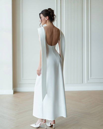 Woman wearing a white dress with a backless design in a minimalistic setting.