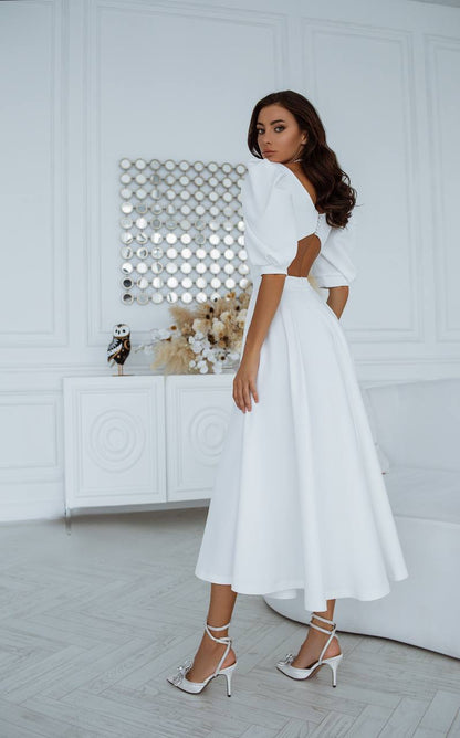 Woman in a white dress standing in a minimalistic room with a decorative wall.