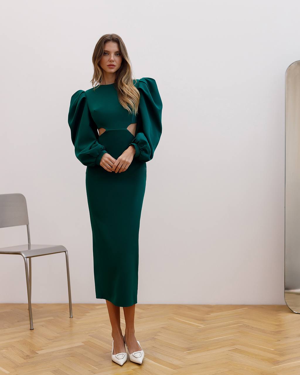 Woman wearing a green dress with puff sleeves in a minimalistic room.