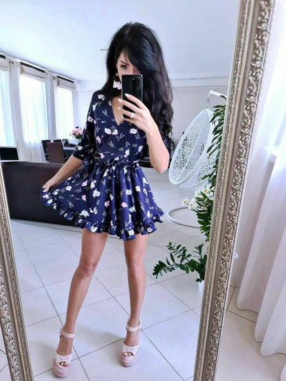 Woman taking a mirror selfie wearing a navy blue floral dress in a bright room.