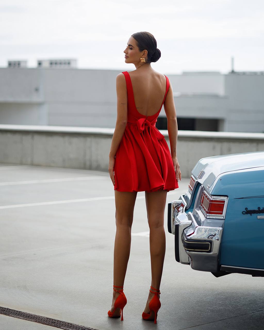 Woman in a red dress standing on a rooftop with a vintage car in the background