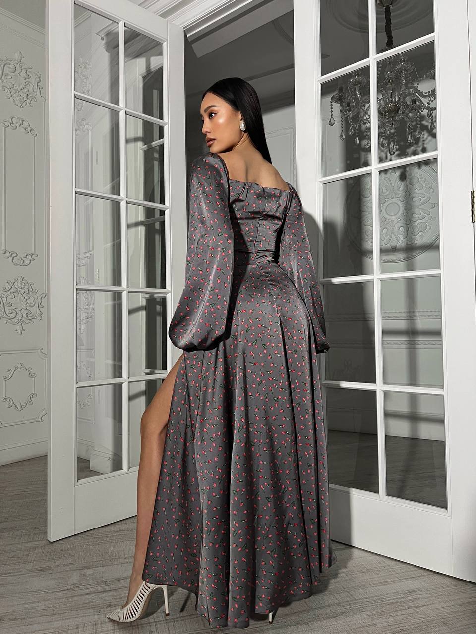 Woman in a long, patterned dress standing in a room with large glass doors.