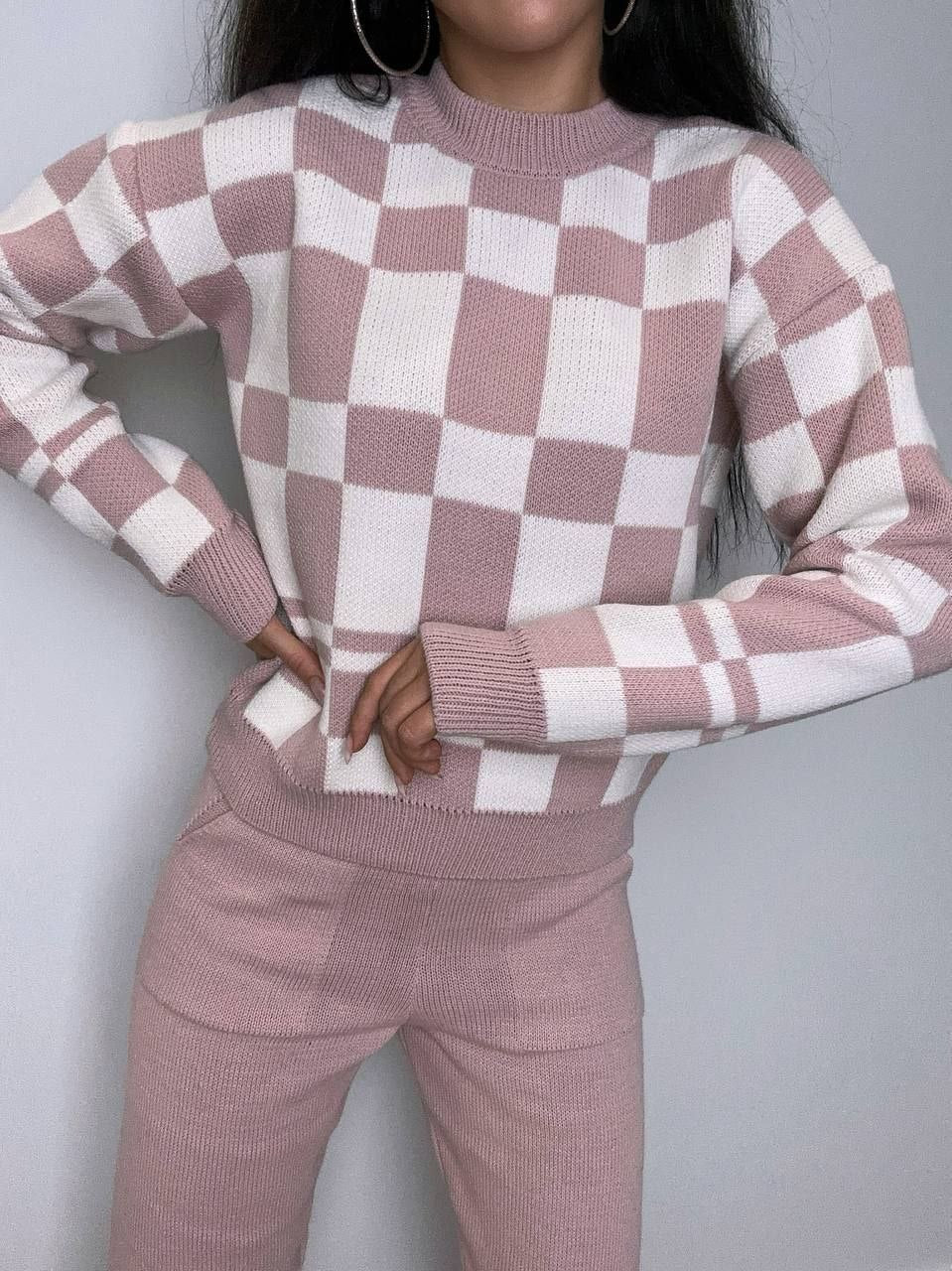 Person wearing a pink and white checkered sweater and pants against a gray background