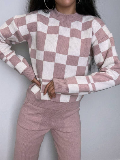 Person wearing a pink and white checkered sweater and pants against a gray background