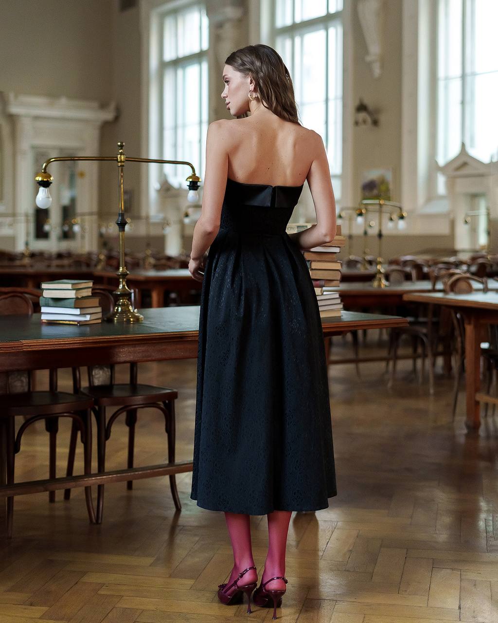 Woman in a black dress standing in a large room with wooden tables and chairs.