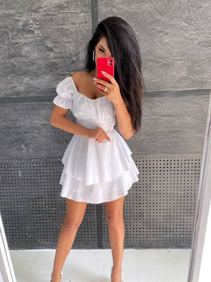 Woman taking a mirror selfie wearing a white dress against a gray wall.