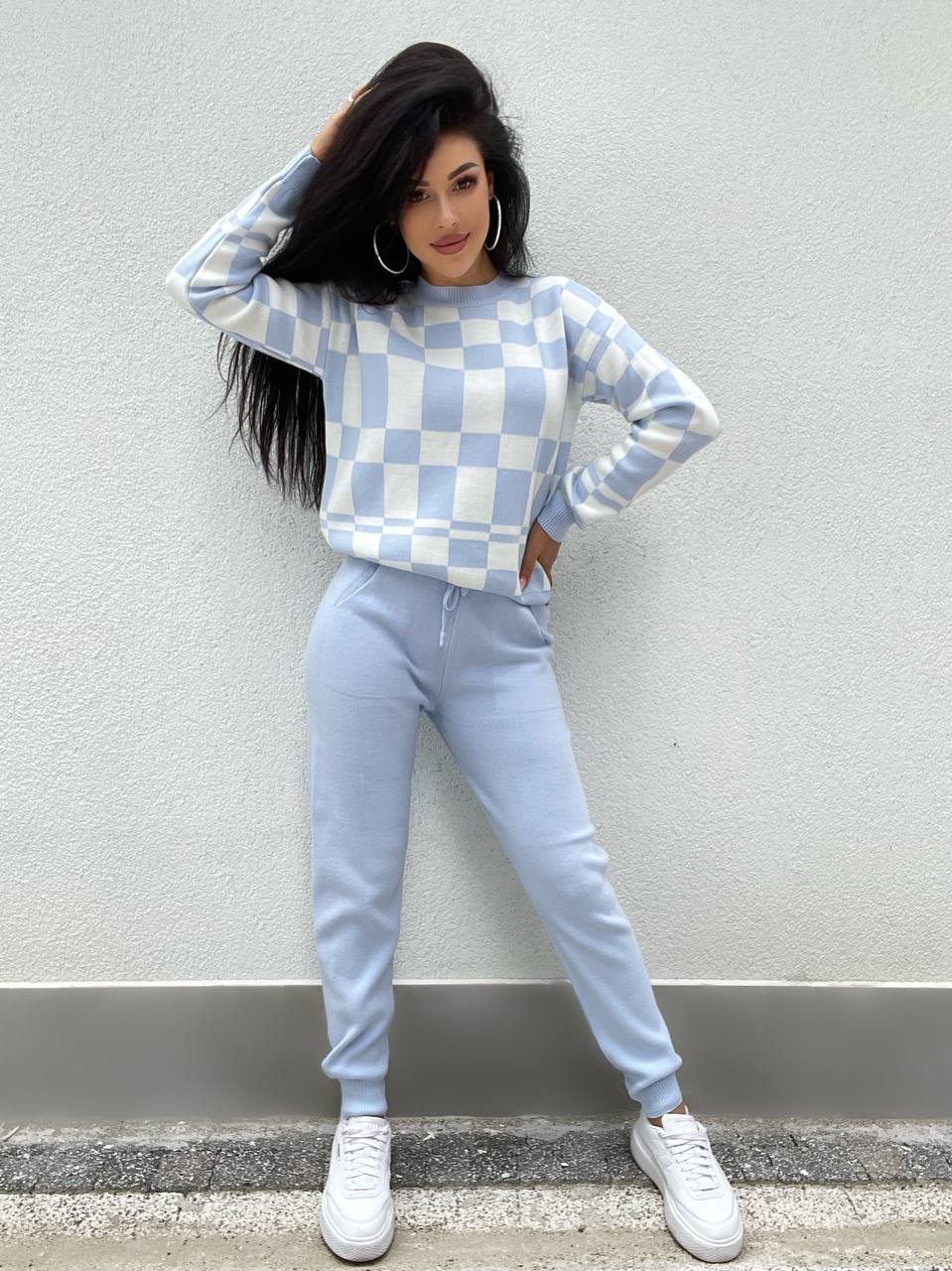 Person wearing a checkered sweater and light blue pants against a plain background