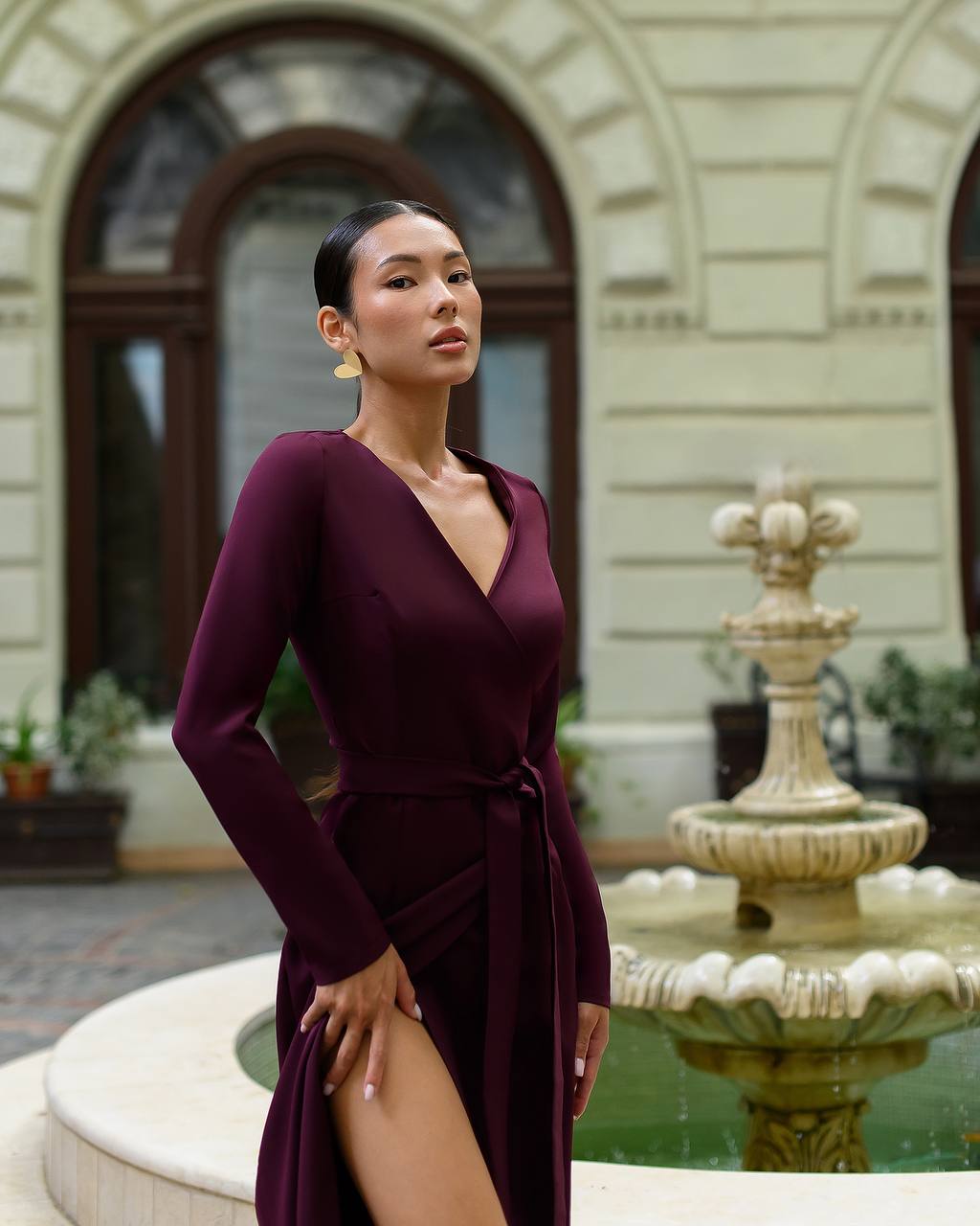 Woman in a burgundy dress standing in front of a fountain with classical architecture.