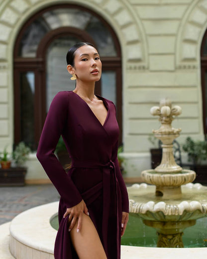 Woman in a burgundy dress standing in front of a fountain with classical architecture.