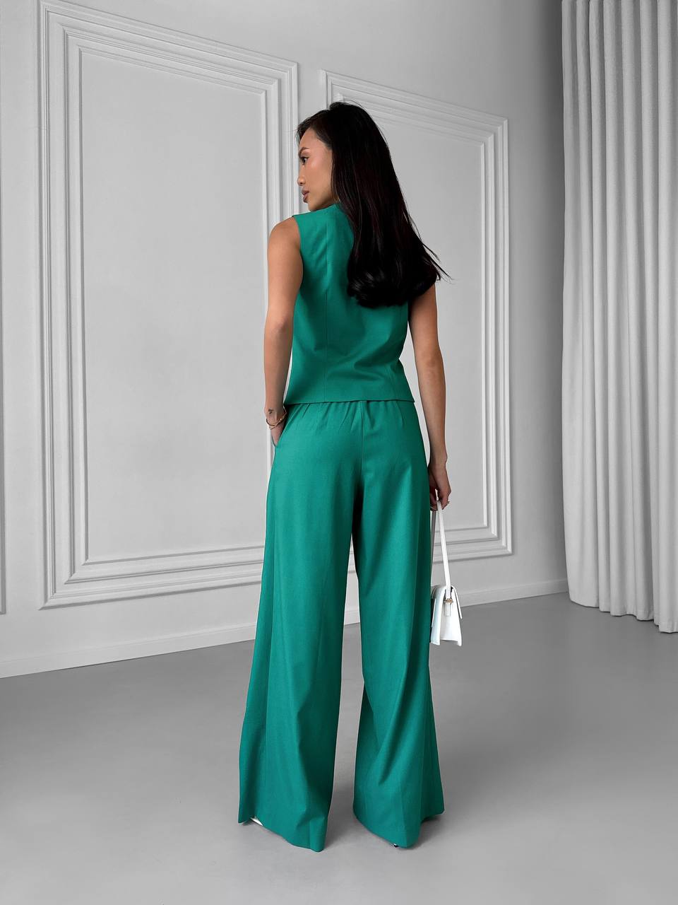 Woman wearing a green jumpsuit standing against a gray wall.