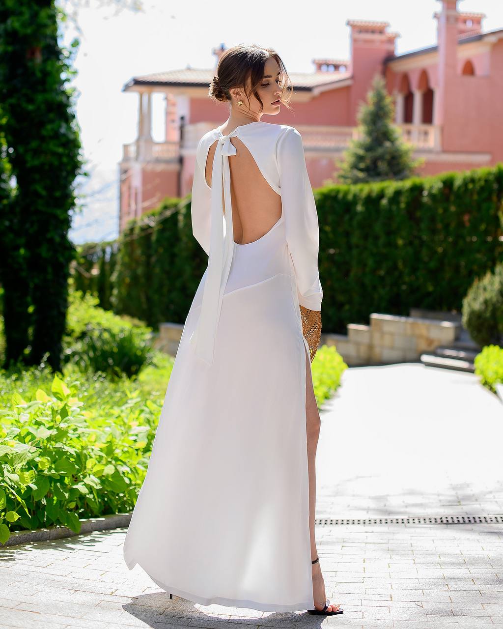 Woman in a white dress with a backless design walking outdoors.
