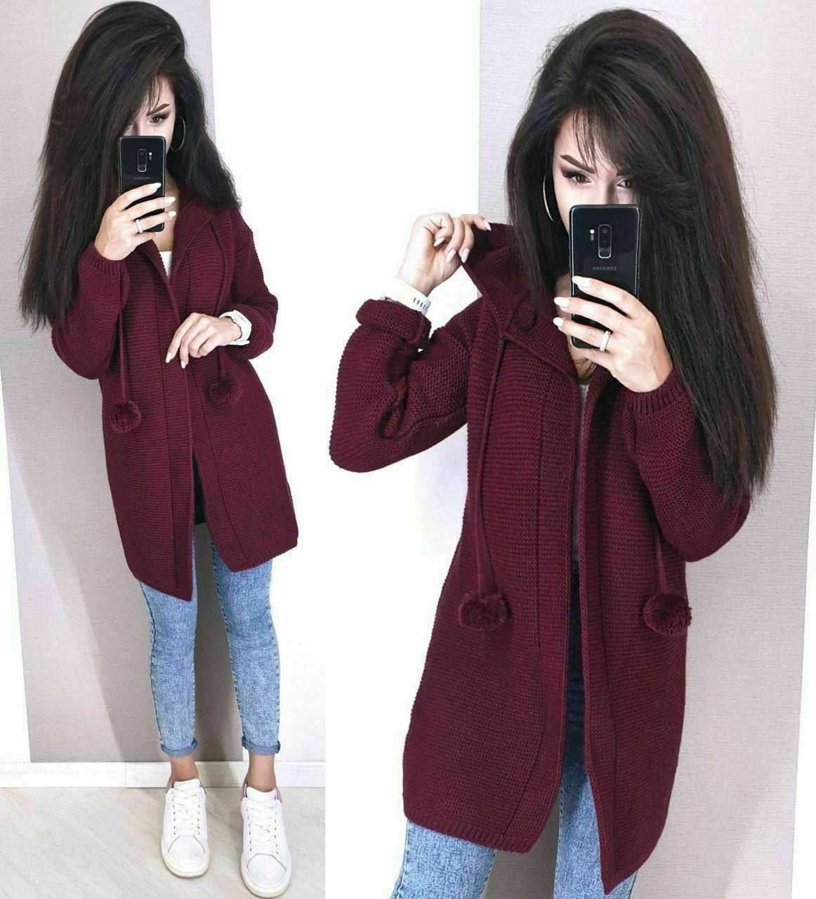 Woman wearing a burgundy coat with pom-pom details, taking a mirror selfie.