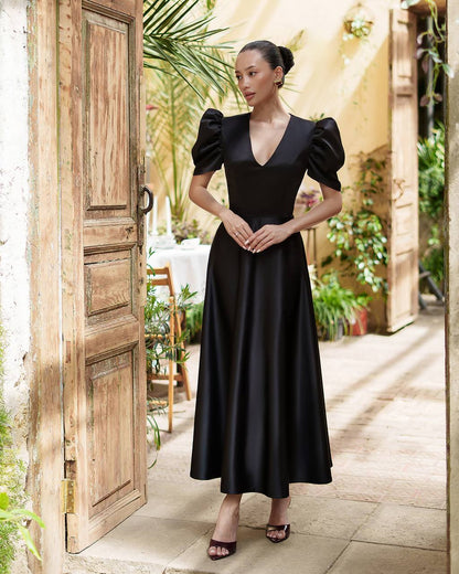 Woman in a black dress standing in an outdoor setting with wooden doors and plants.