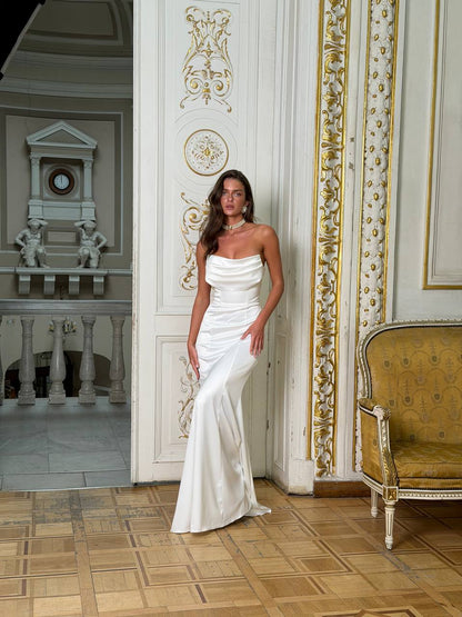 Woman in a white strapless gown standing in an ornate room with decorative walls and a chair.