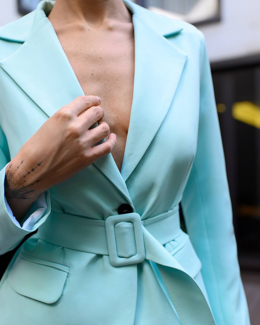Light blue blazer with a belt being adjusted against a blurred background