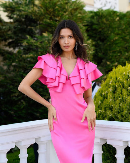 Woman wearing a bright pink dress with ruffled sleeves standing outdoors.