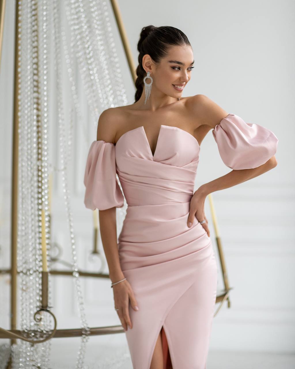 Woman wearing a pink off-shoulder dress with puffed sleeves in an elegant setting.