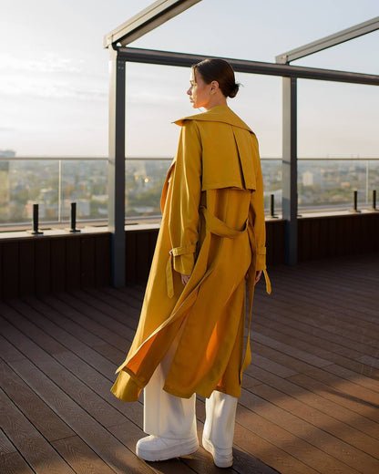 Person wearing a yellow trench coat on a rooftop with a cityscape view.