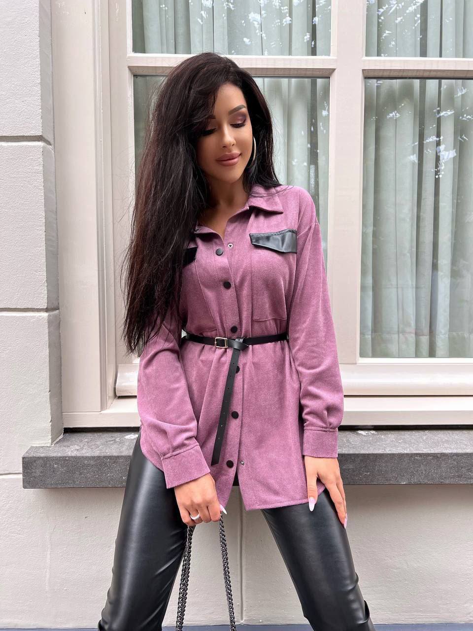 Woman wearing a pink coat and black leather pants standing in front of a window.