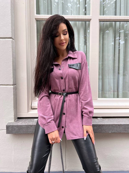 Woman wearing a pink coat and black leather pants standing in front of a window.