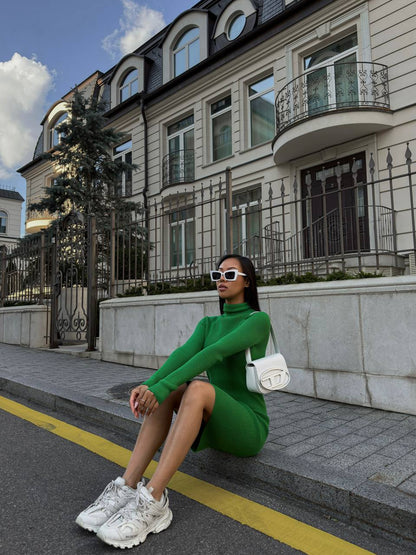 Woman in a green dress sitting on a sidewalk in front of an elegant building.