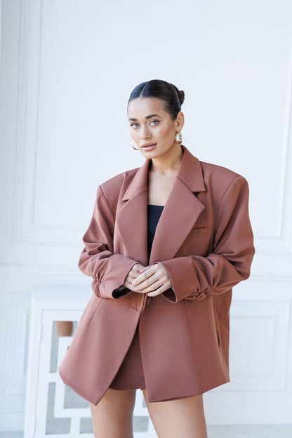 Woman wearing a brown blazer over a black top against a white background