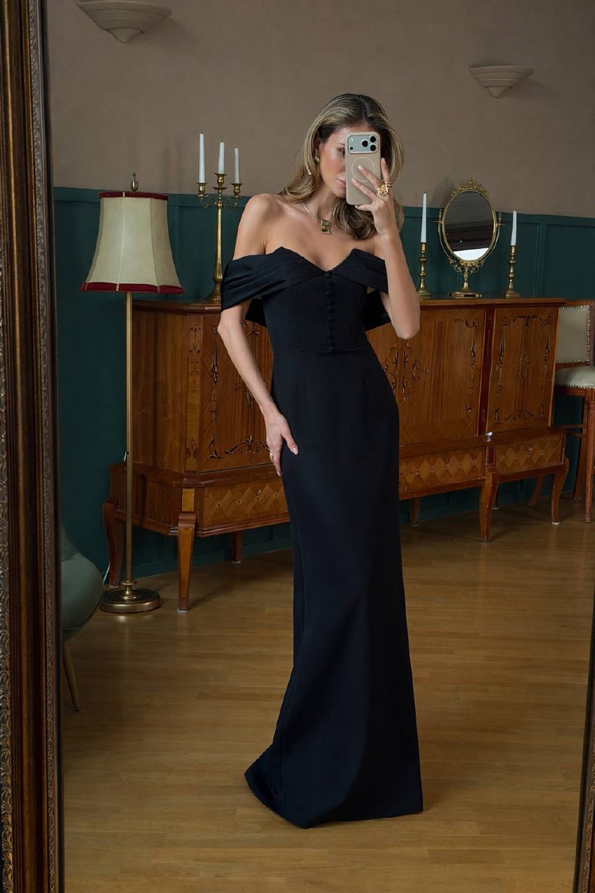 Woman in a black off-shoulder gown taking a mirror selfie in an elegant room.